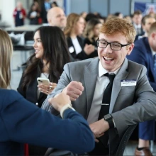 Students wearing business formal attire chatting at an in-person event.