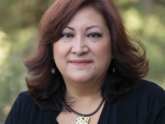 Photo of Dr. Retis in front of blurred green foliage 